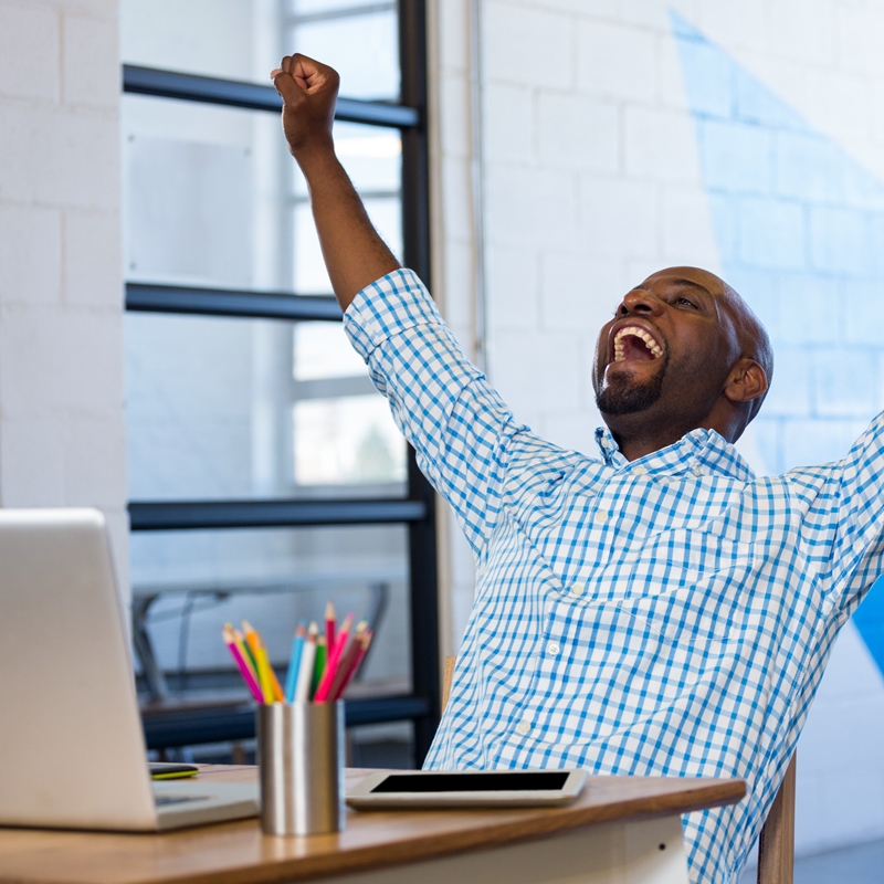 Excited man sitting on table with digital tablet and laptop in office